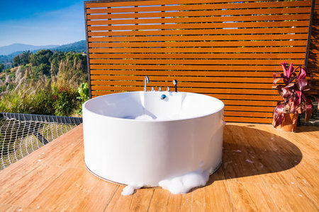 Phetchabun, Thailand - January, 06, 2025 : Outdoor Bathing Retreat with White Tub on Elegant Wooden Deck Surrounded by Nature at Phetchabun, Thailand.の写真素材