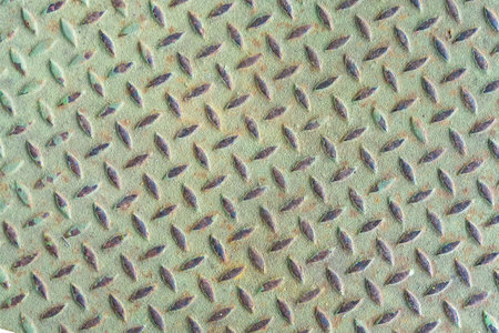Close-up of a weathered and rusty metal diamond plate with raised patterns and textured surfaceの写真素材