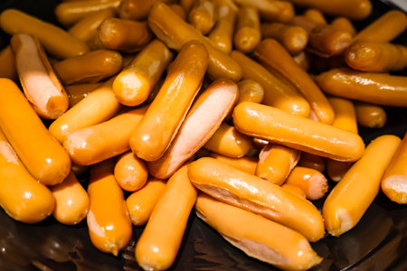 A heap of yellow cocktail sausages closely stacked together, highlighting their smooth texture and shiny appearanceの写真素材