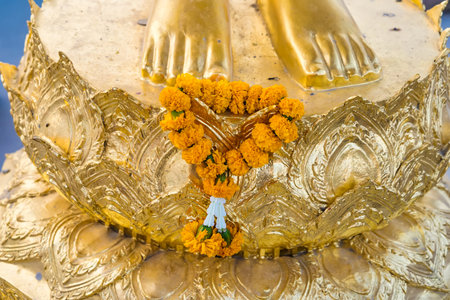 Close-up view of golden Buddha statue's feet decorated with a vibrant marigold flower garland.の写真素材