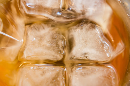 Close-up of ice cubes in a glass of iced tea, emphasizing a refreshing, cold beverage with a golden brown hueの写真素材