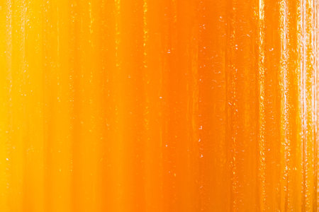 Close-up view of vibrant orange texture with vertical lines and subtle reflections creating a dynamic abstract backgroundの写真素材