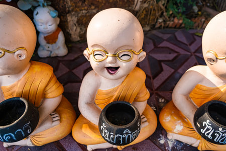 Lop Buri, Thailand - January, 02, 2025 :Colorful ceramic monk statues in orange robes holding alms bowls displayed on a stone surface in bright daylight at Lop Buri, Thailandの写真素材