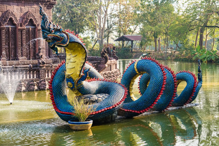Lop Buri, Thailand - January, 02, 2025 : Ornate giant serpent statue in a serene park pond surrounded by lush green trees on a sunny day at Lop Buri, Thailand.の写真素材