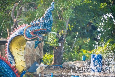 Lop Buri, Thailand - January, 02, 2025 : Ornate giant serpent statue in a serene park pond surrounded by lush green trees on a sunny day at Lop Buri, Thailand.の写真素材