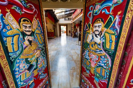 Ayutthaya, Thailand - March, 10, 2025 : Traditional Chinese temple doors with vibrant guardian deity paintings open to reveal an ornate interior space at Ayutthaya, Thailandの写真素材
