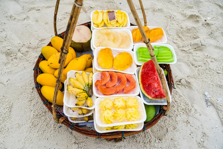 Assorted fresh tropical fruits displayed in a basket on sandy beach backgroundの写真素材