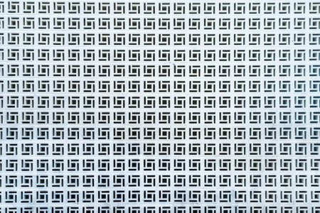 White geometric perforated wall with repetitive square patterns creating a symmetrical and abstract designの写真素材