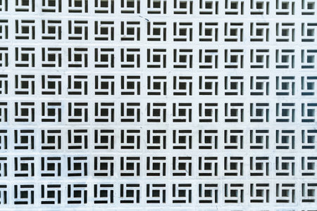 White geometric perforated wall with repetitive square patterns creating a symmetrical and abstract...