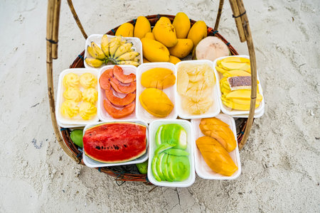 Assorted fresh tropical fruits displayed in a basket on sandy beach backgroundの写真素材