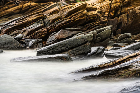 Photo long exposure of Rocky shoreline with jagged rocks extending into the calm sea under a cloudy sky, creating a serene coastal landscapeの写真素材