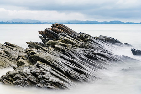 Photo long exposure of Rocky shoreline with jagged rocks extending into the calm sea under a cloudy sky, creating a serene coastal landscapeの写真素材