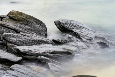 Photo long exposure of Rocky shoreline with jagged rocks extending into the calm sea under a cloudy sky, creating a serene coastal landscapeの写真素材