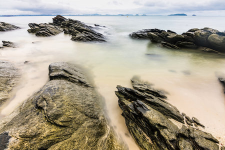 Photo long exposure of Rocky shoreline with jagged rocks extending into the calm sea under a cloudy sky, creating a serene coastal landscapeの写真素材