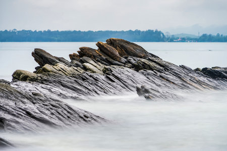 Photo long exposure of Rocky shoreline with jagged rocks extending into the calm sea under a cloudy sky, creating a serene coastal landscapeの写真素材