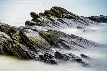 Photo long exposure of Rocky shoreline with jagged rocks extending into the calm sea under a cloudy sky, creating a serene coastal landscapeの写真素材