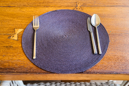 A woven placemat with a fork, knife, and spoon arranged on a wooden table ready for diningの写真素材