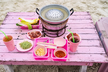 Beachside setup with a grill, pink table, drinks, and beanbags overlooking the sea, creating a relaxing outdoor dining atmosphereの写真素材