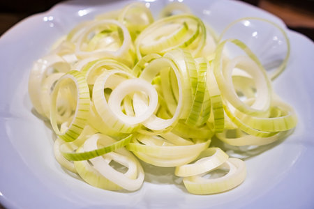 A white plate filled with fresh, vibrant slices of leeks, showing their green and white layers, ready for cooking or garnishingの写真素材