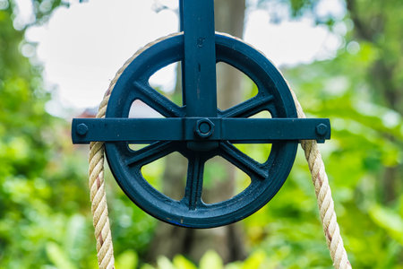 Close-up of a metal pulley with a rope set against a vibrant green natural background in an outdoor settingの写真素材