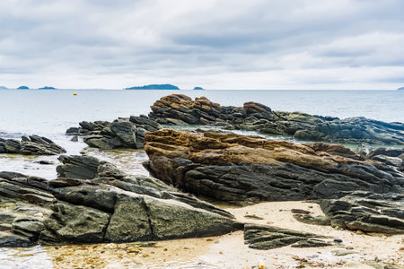 A rocky shoreline on a cloudy day with distant islands in view across the calm sea watersの写真素材