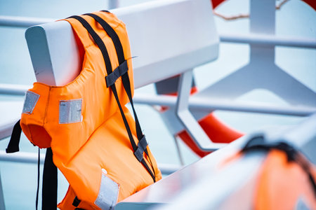 Bright orange life jacket draped over a modern boat bench, with a blurred lifebuoy ring visible in...