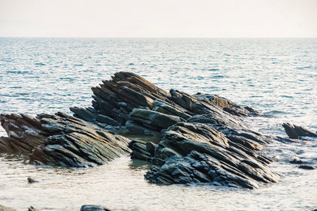 Jagged rock formations extend into the calm sea under a clear sky, showcasing a serene coastal landscapeの写真素材