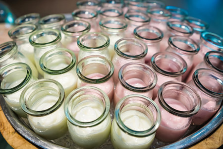 Close-up of multiple small glass jars filled with white and pink yogurt arranged on a tray in an inviting displayの写真素材