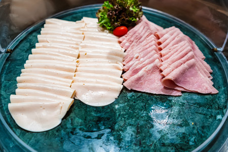 Sliced turkey and ham arranged neatly on a platter with lettuce and cherry tomato garnish in a buffet settingの写真素材