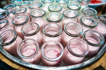 Close-up of multiple small glass jars filled with white and pink yogurt arranged on a tray in an inviting displayの写真素材