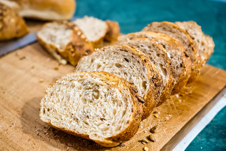 Sliced whole grain bread arranged on a wooden board with visible bread crumbs and a blue backgroundの写真素材