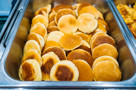 A large tray filled with a stack of freshly cooked small pancakes displayed in a buffet setting, ready to be served.の写真素材