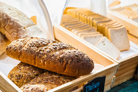 Freshly baked whole grain bread loaves covered with seeds displayed in a wooden basket at a bakery