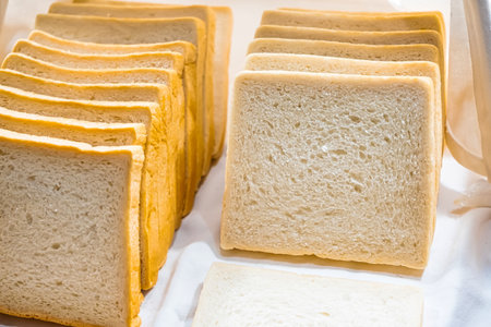 Freshly sliced bread displayed in wooden trays at a bakery with a pair of tongs beside the loaves