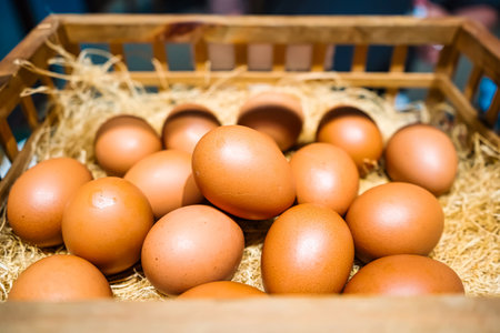 A wooden basket filled with fresh brown eggs nestled in straw, captured in a close-up view.の写真素材