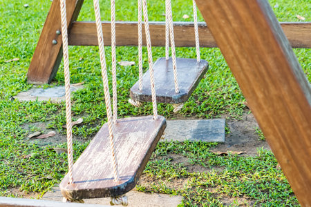 Two wooden swings suspended by ropes on a wooden frame in a grassy outdoor playground.