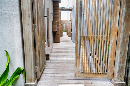 Wooden pathway leading through a modern rustic building with open gates and greenery on the side.の写真素材