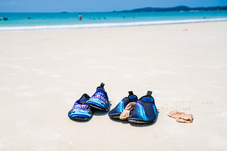 Rayong, Thailand - April, 01, 2025 : View of a tranquil beach with blue water shoes and sandals on sandy shore under a clear blue skyの写真素材