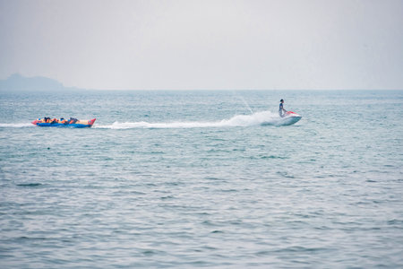 Rayong, Thailand - April, 01, 2025 : Person riding a jet ski towing a banana boat with a group of...
