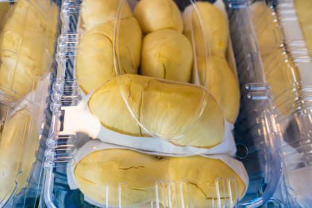 Close-up of durian fruit neatly packed in a clear plastic container, showcasing bright yellow flesh and white edible seedsの写真素材