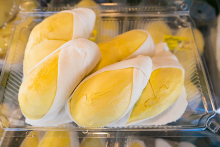 Close-up of durian fruit neatly packed in a clear plastic container, showcasing bright yellow flesh and white edible seedsの写真素材