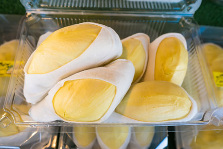 Close-up of durian fruit neatly packed in a clear plastic container, showcasing bright yellow flesh and white edible seedsの写真素材