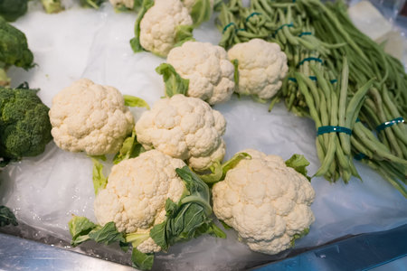 Fresh cauliflower heads and green beans arranged on ice at a market stall showcasing fresh vegetablesの写真素材