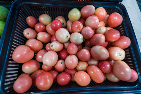 Basket of ripe red tomatoes on display at a market stall, showcasing fresh produce ready for purchaseの写真素材