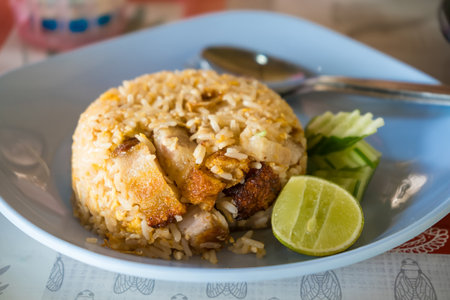 Delicious serving of Thai chicken fried rice with fresh lime and cucumber slices on a blue plate with a spoon.の写真素材