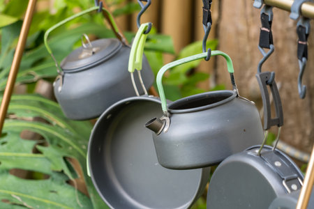 Camping kitchen gear including kettles and pots hanging on a portable drying rack outside near trees...