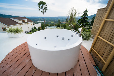 Outdoor round bathtub on a patio with scenic lush greenery and pine trees in the background, featuring sleek design and modern architectureの写真素材