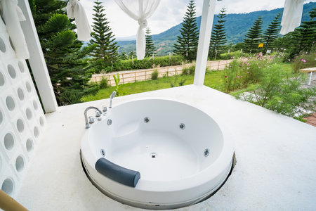Outdoor round bathtub on a patio with scenic lush greenery and pine trees in the background, featuring sleek design and modern architectureの写真素材