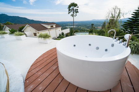 Outdoor round bathtub on a patio with scenic lush greenery and pine trees in the background, featuring sleek design and modern architectureの写真素材