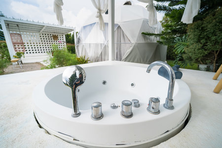Outdoor round bathtub on a patio with scenic lush greenery and pine trees in the background, featuring sleek design and modern architectureの写真素材
